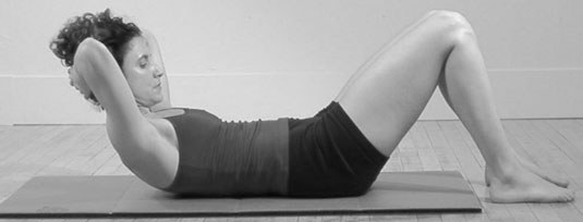 Exhale: Pull the navel in toward the spine and lift your head, pulling your chin in toward your chest as if you are squeezing a tangerine under your chin, as you roll up to your Pilates Abdominal Position.