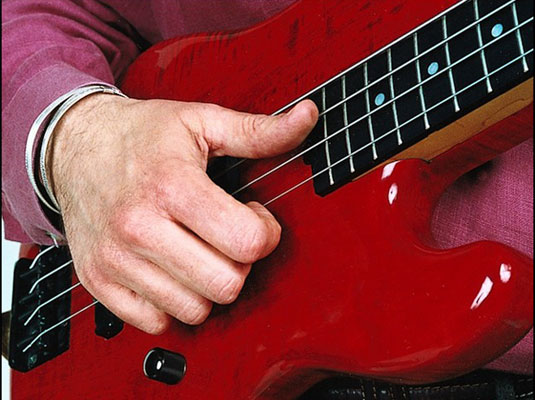 With a sharp twist of your wrist, flick your thumb against one of the low strings, striking it at the very end of the fingerboard.