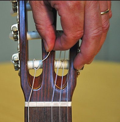 Bring the end of the string back over the roller toward you; then pass the string under itself in front of the hole.