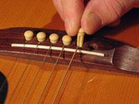 Wedging the bridge pin back into the acoustic guitar.