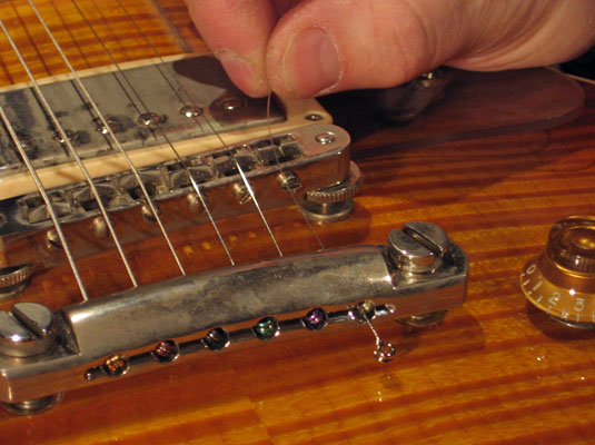 <b>Anchor the string at the bridge by passing the string through the hole (from the back or bottom of the guitar) until the ball stops the movement.</b>