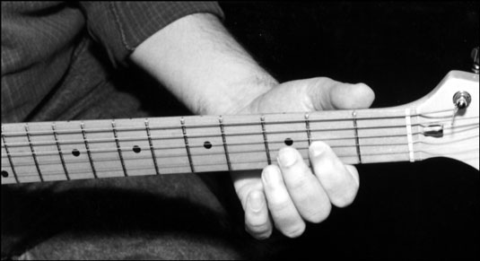 The electric guitar neck lies comfortably between the thumb and the first finger as the first finge