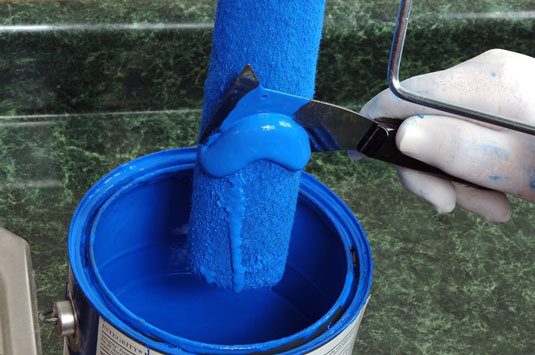 Put on your gloves and scrape off excess paint from the roller.