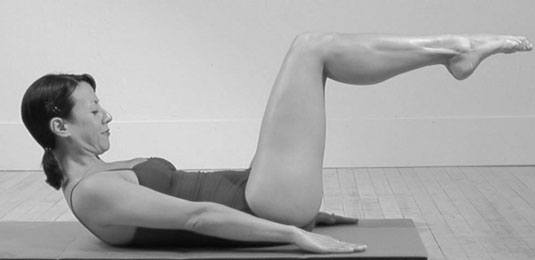 Exhale: As you reach your arms back down to the floor, lift your head and roll up to the Pilates Abdominal Position with your shoulder blades just off the mat.