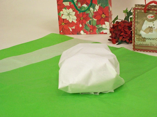 Place three or four sheets of tissue paper on a flat surface, overlapping each sheet by a few inches; place the gift in the middle.