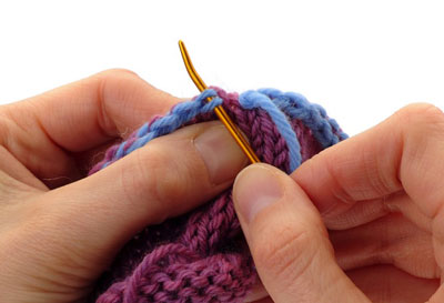 Thread the yarn tail onto a seaming needle. Insert the seaming needle from front to back under both legs of the V that constitutes the first bound-off stitch of the round. Pull the needle through and snug up this stitch.