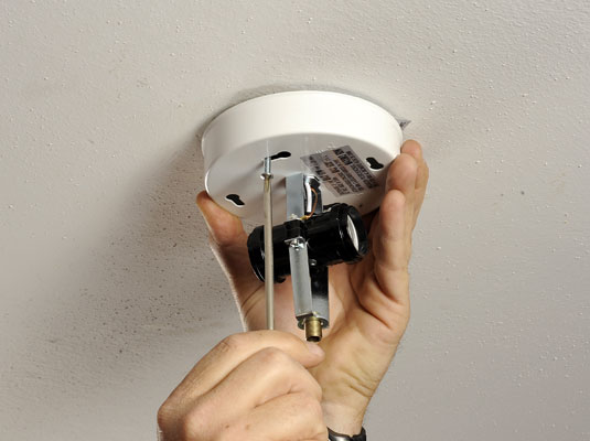 Unscrew the screws or nuts holding the fixture base to the ceiling box.