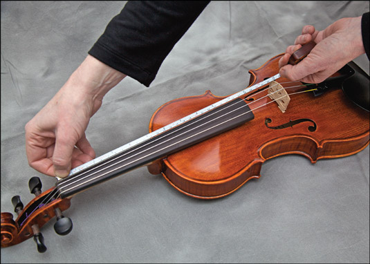 Measuring the vibrating length of the A string. [Credit: Photograph by Nathan Saliwonchyk]