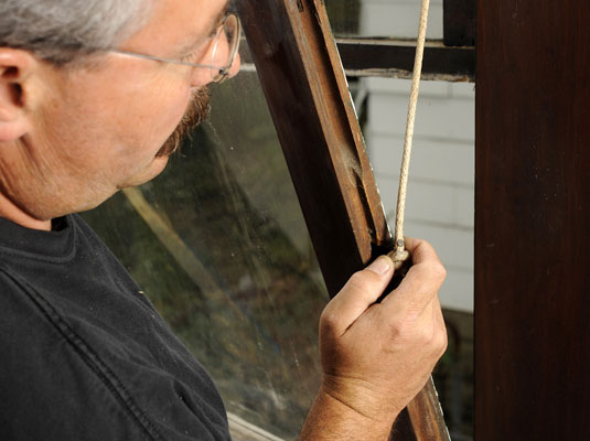 Detach the cord from its slot on each side of the lower sash.