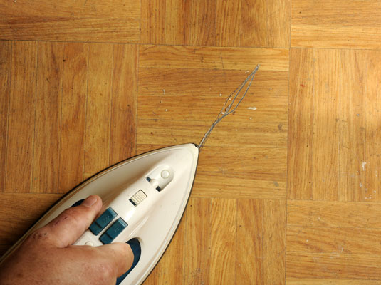 Apply heat to the damaged tile with the heat gun or warm iron to soften the adhesive underneath.