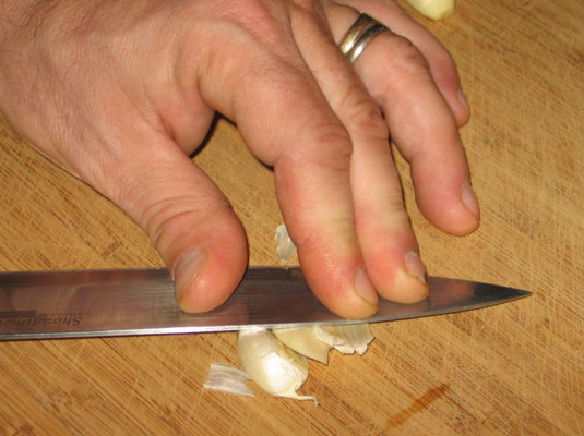 Break off a clove, put it on a cutting board, and smack it with the flat side of your chef’s knife.