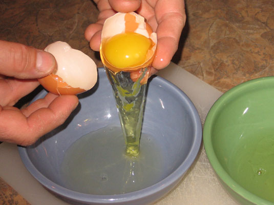 Carefully pass the yolk back and forth from one shell cavity to the other, releasing a little more white into the bowl.