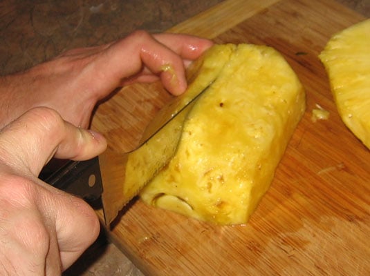 Place a pineapple half on the cutting board and cut that half in half, lengthwise.