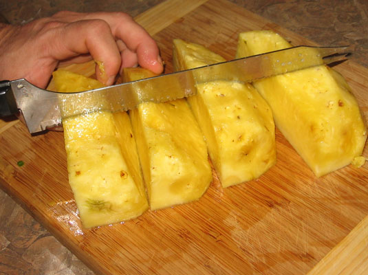 With the pineapple quarters together, cut them perpendicular to the length.