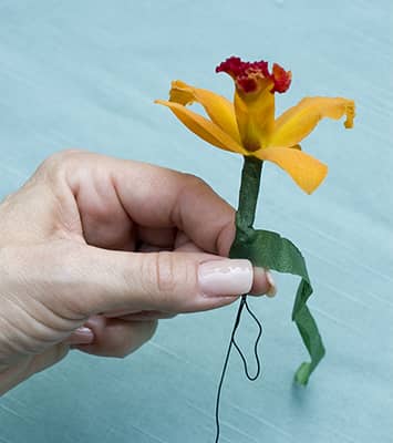 flower with florist's wire around it in hand of corsage maker