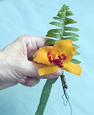 fern frond added to flower in hand of corsage maker