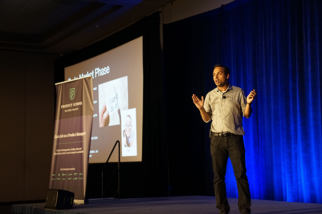 Man speaking onstage next to a projected image