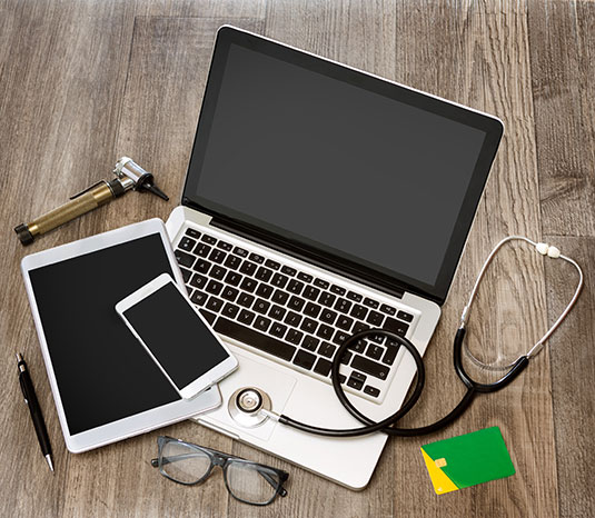 eyeglasses, stethoscope, otoscope, pen, ID badge, mobile phone, tablet, and laptop on desk