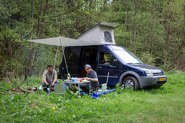 Photo showing two people cooking outside near their small pop-top camper van