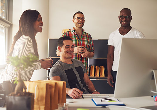 Diverse group of four Black, Hispanic and Caucasian young adult entrepreneurs together in front of computer monitor on desk at small business office