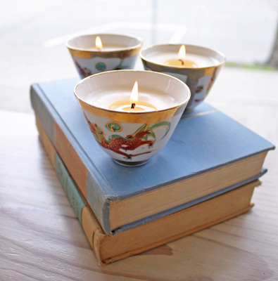 Photo showing tea cups that have been upcycled into candles, sitting atop two old books.